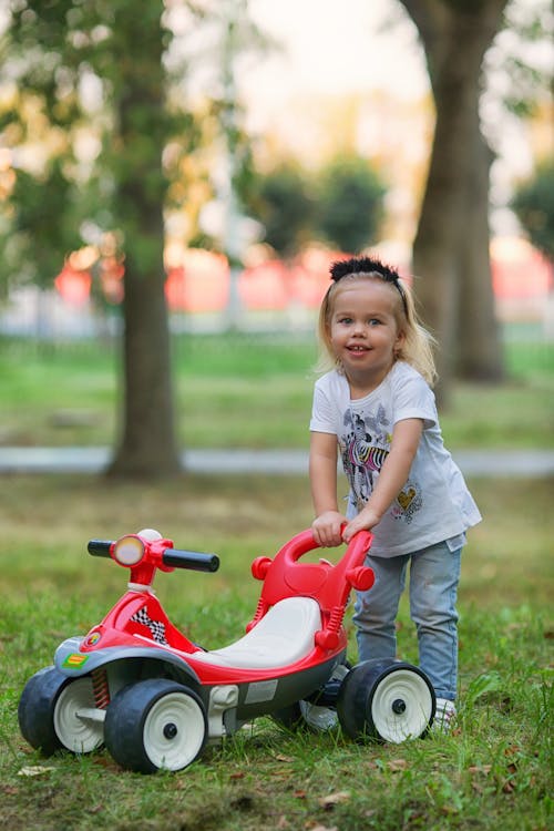 Girl in White T-shirt Standing Behind Red Toy Vehicle