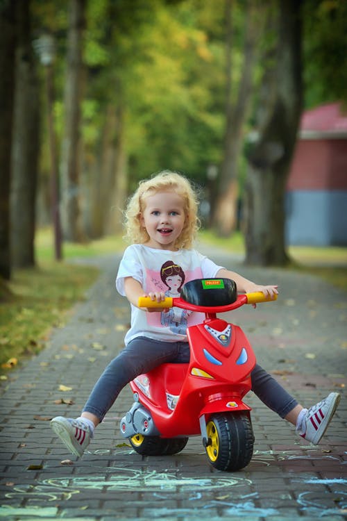 Girl Riding Red Scooter on Pavement with Chalk Drawings