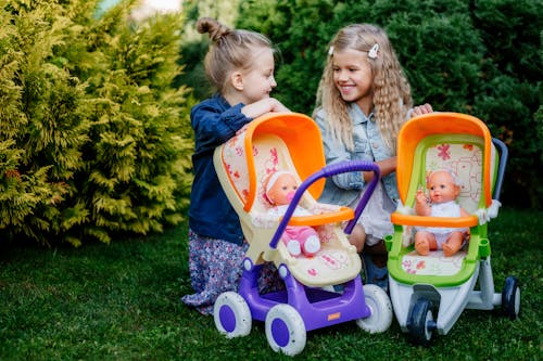 Two Girls Sitting Behind Two Toy Strollers with Dolls