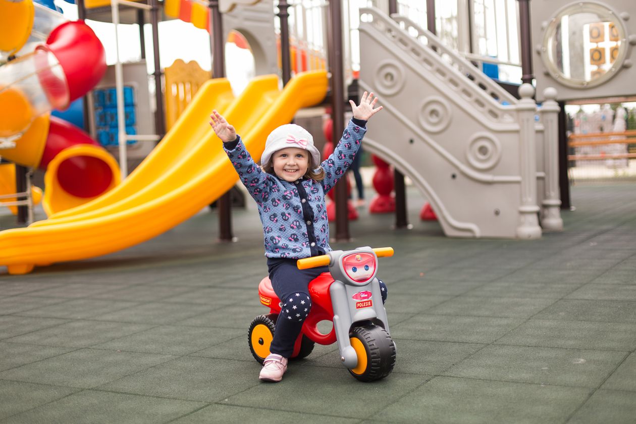 Toddler riding a low push scooter toy outdoors, a toy for new walkers