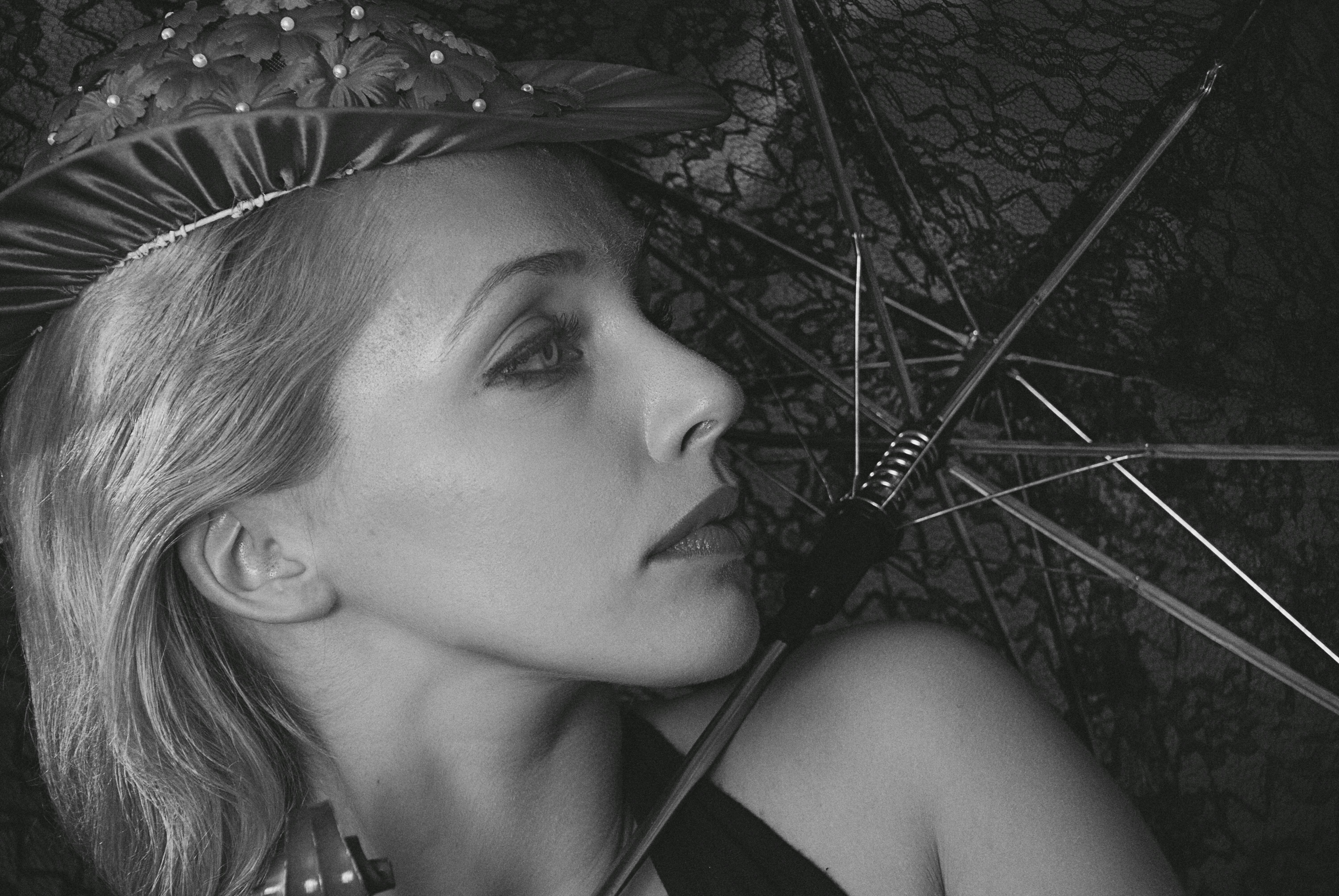 Sophisticated black and white portrait of a woman wearing a decorative hat, posing with an umbrella.