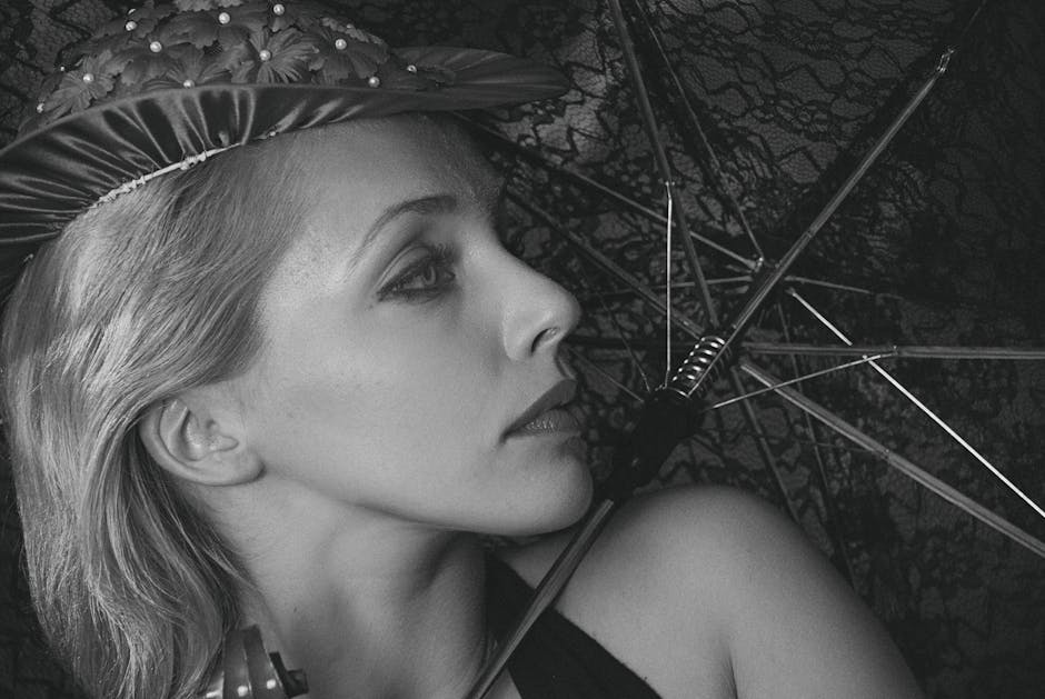 Sophisticated black and white portrait of a woman wearing a decorative hat, posing with an umbrella.