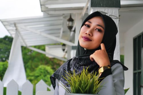 Free Elegant woman in hijab with makeup posing outdoors in front of a white house, exuding confidence and style. Stock Photo