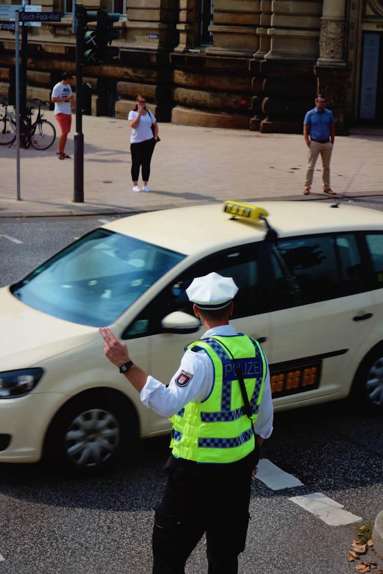 Policeman In Green Vest Directing Traffic On The Road