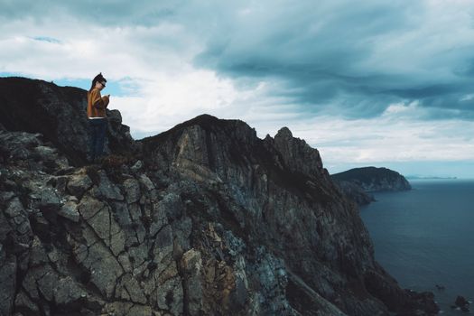Dramatic scene of a woman standing on a rocky cliff by the sea under a cloudy sky.