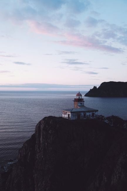Serene lighthouse on a rugged cliff by the sea during sunset, with soft pastel skies.