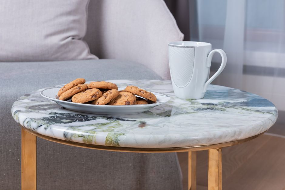 White ceramic mug with hot drink placed on marble table with plate of tasty cookies with chocolate