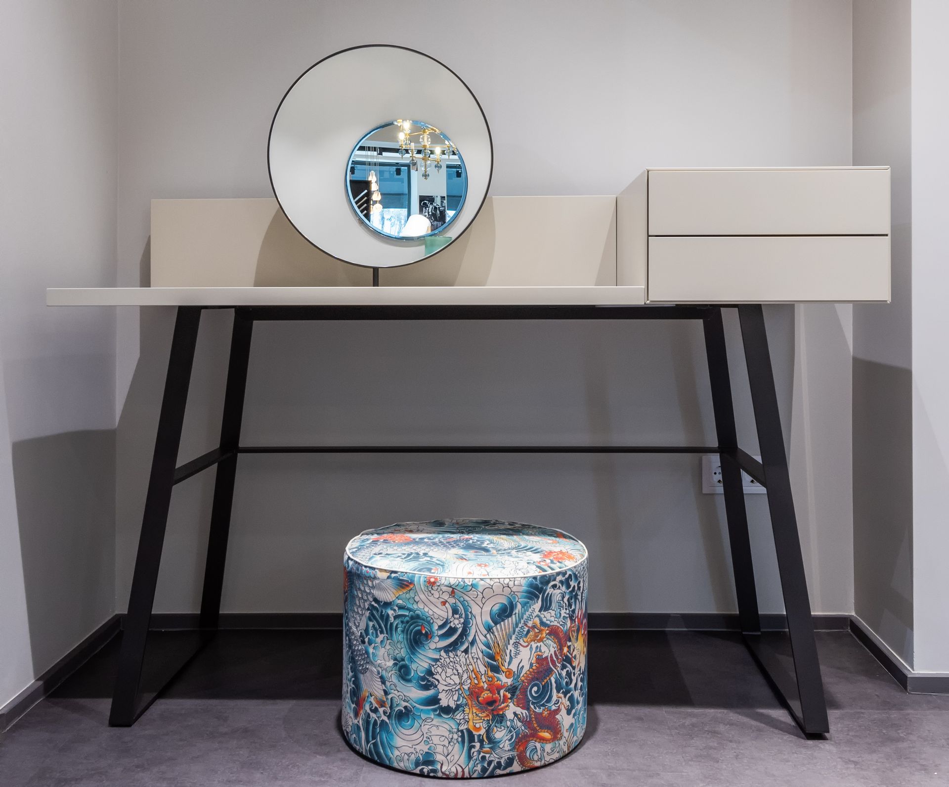 Stylish vanity desk with round mirror and colorful pouf in a contemporary setting.