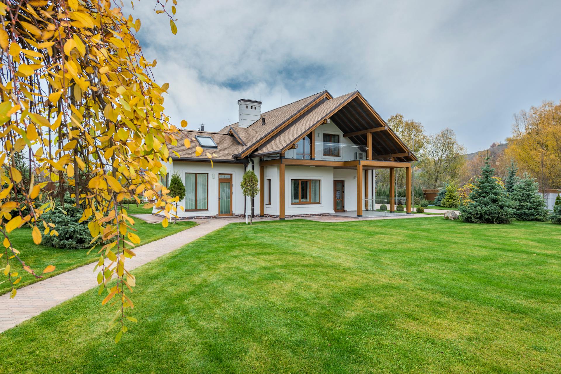 Exterior of residential suburban cottage with balcony surrounded with lush green plants and trees