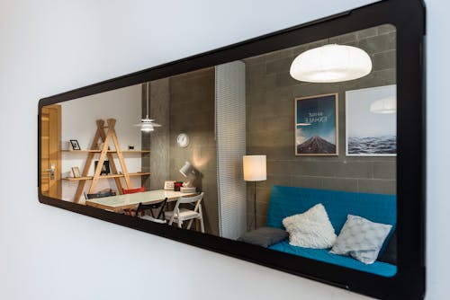 Interior of cozy modern living room with comfortable couch and big table reflected in narrow long mirror