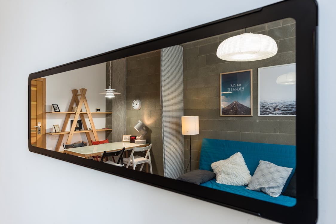 Interior of cozy modern living room with comfortable couch and big table reflected in narrow long mirror