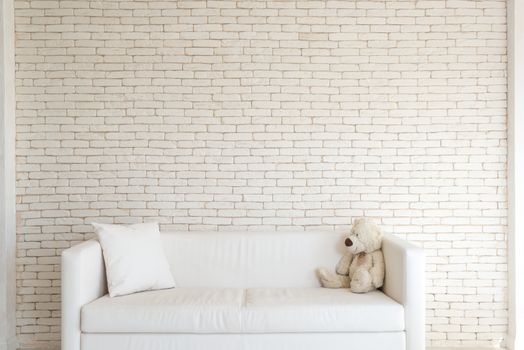 Comfortable white couch with teddy bear and pillow in light room against brick wall