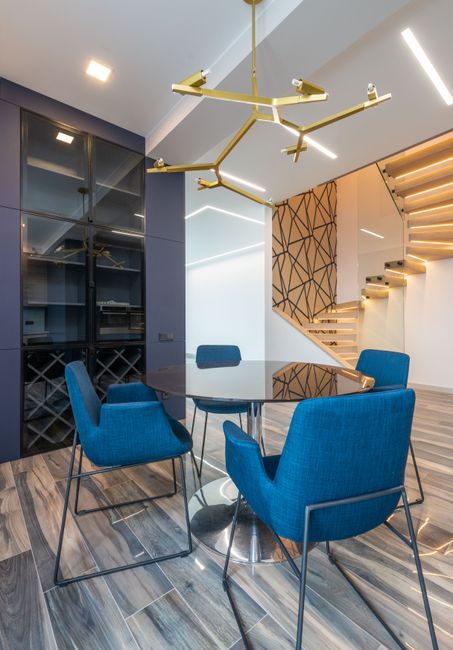 Contemporary dining room highlighted by blue accent chairs, a glass table, and striking overhead lighting.