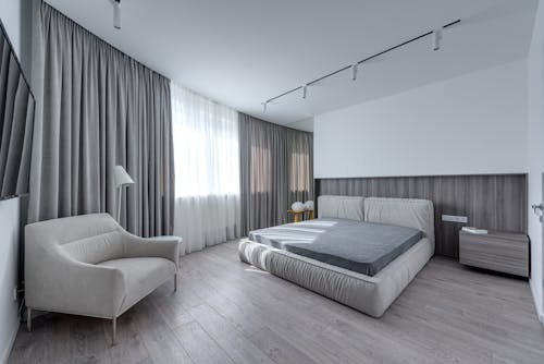 Interior of stylish room with soft bed against TV set and armchair near window in light flat