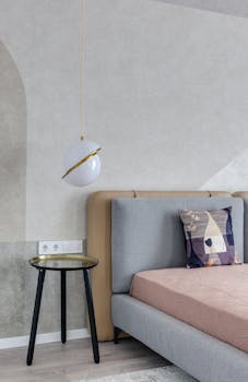 Comfortable bed with colorful pillow near bedside table under lamp with creative design