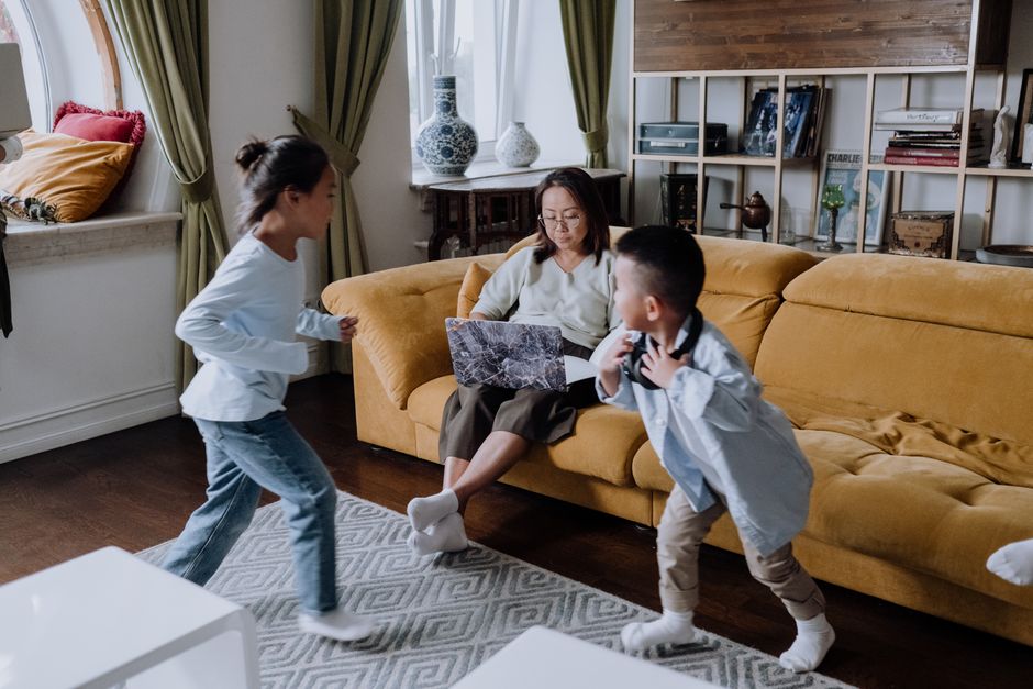 Mother with laptop watching her children play in a cozy living room setting