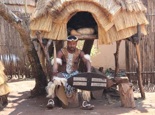 A Man Sitting on a Tree Trunk while Wearing Traditional Clothes