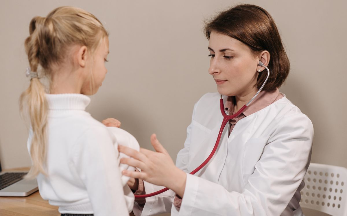 Doctor performing a health check-up on a child using a stethoscope in a clinic setting.