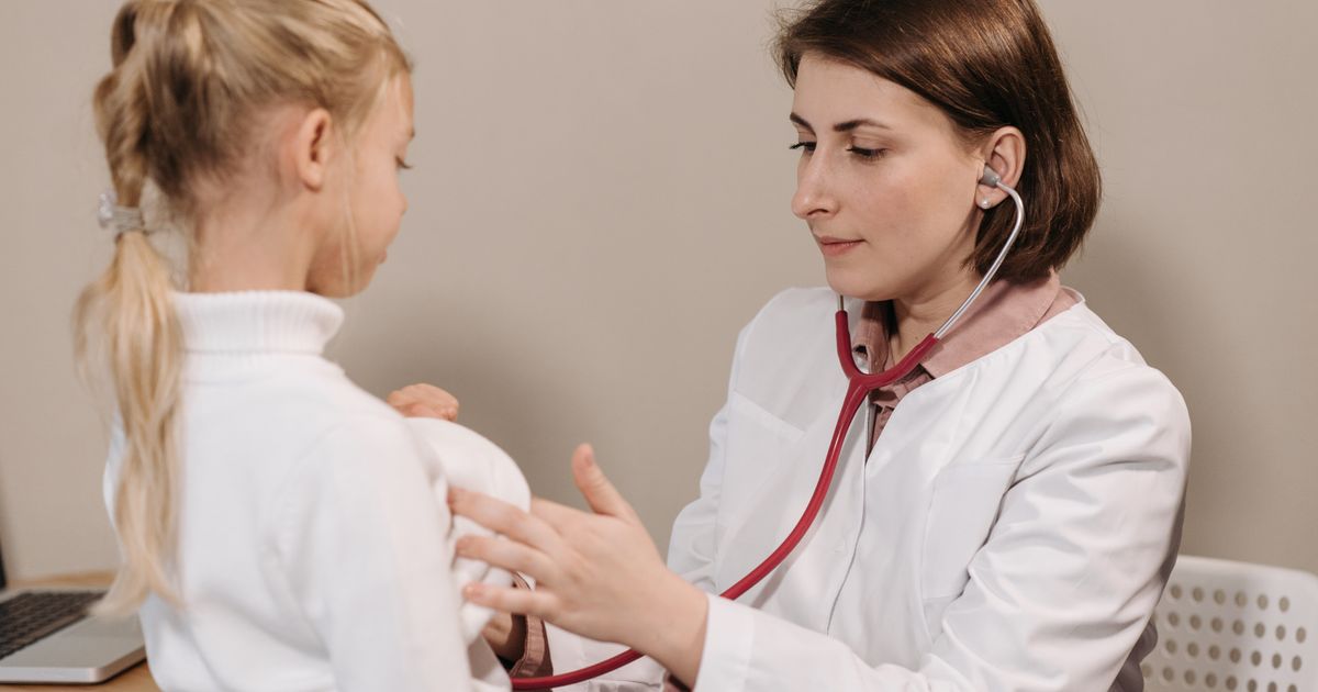 A doctor in a white lab coat examining a young patient with a stethoscope.