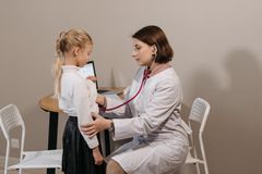 A pediatrician listens to a child's heartbeat during a check-up in a clinic setting.