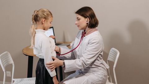 A pediatrician listens to a child's heartbeat during a check-up in a clinic setting.