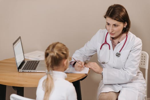 A female doctor listens attentively to a young girl during a medical consultation in an office setting.