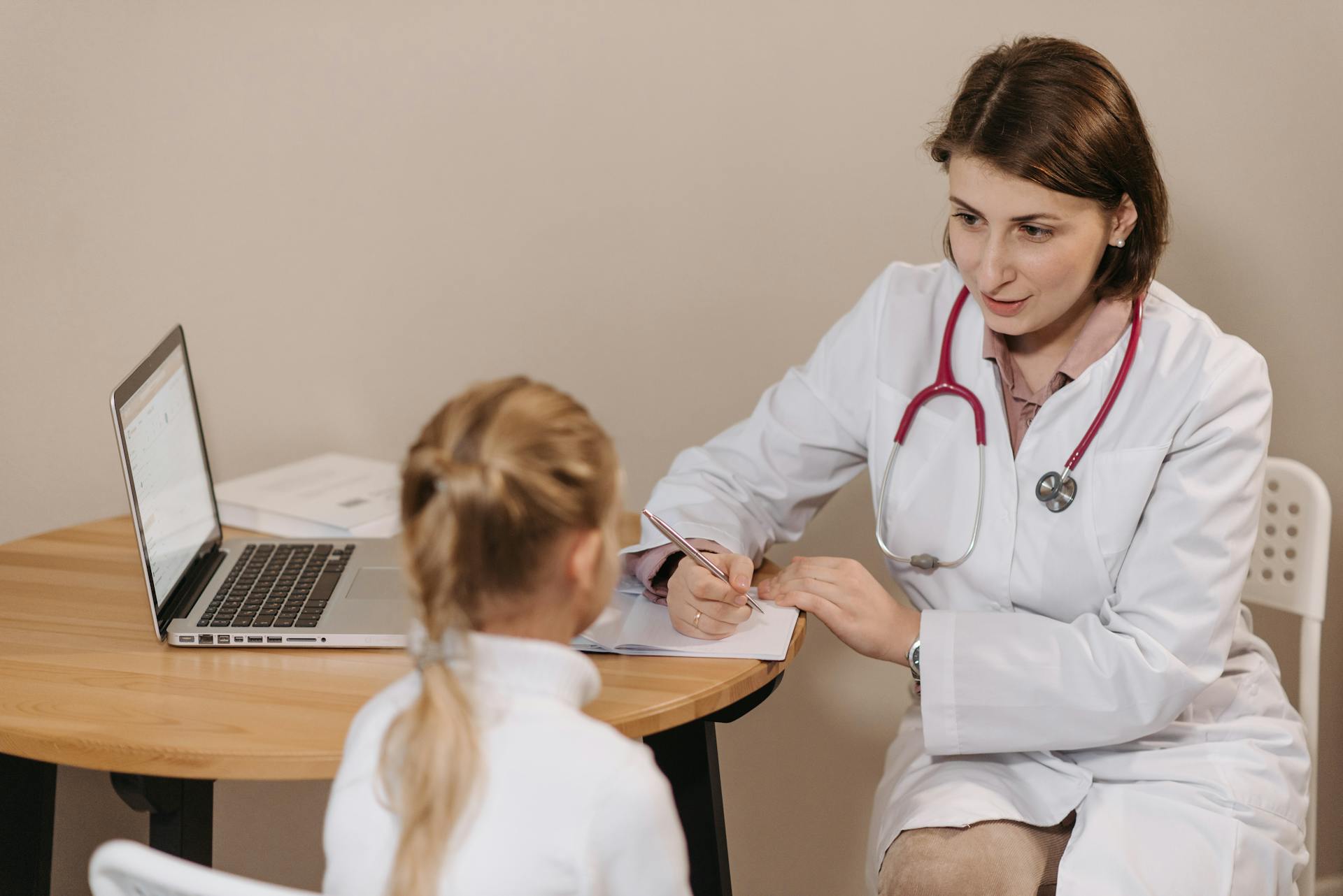 A female doctor listens attentively to a young girl during a medical consultation in an office setting.