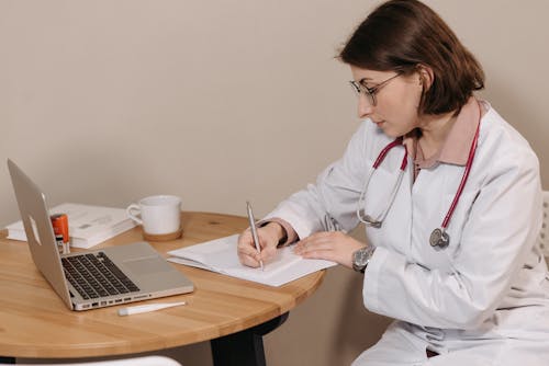 Woman in White Scrub and Eyeglasses Writing on White Paper