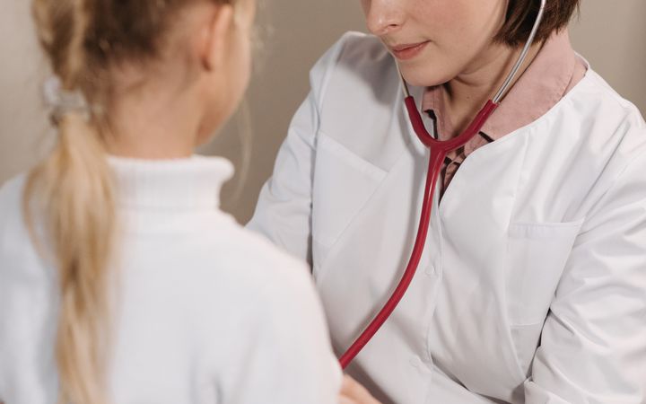 A female doctor examining a child with a stethoscope during a pediatric check-up in a clinic.