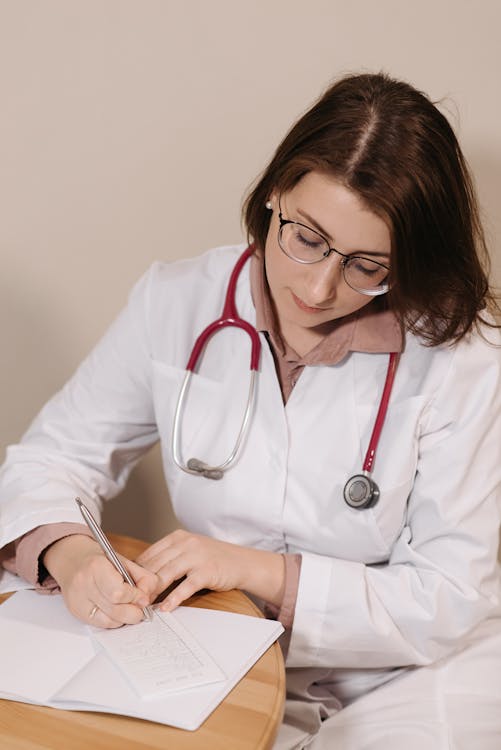 Free Woman in White Scrub and Red Stethoscope Writing Down Prescription Stock Photo
