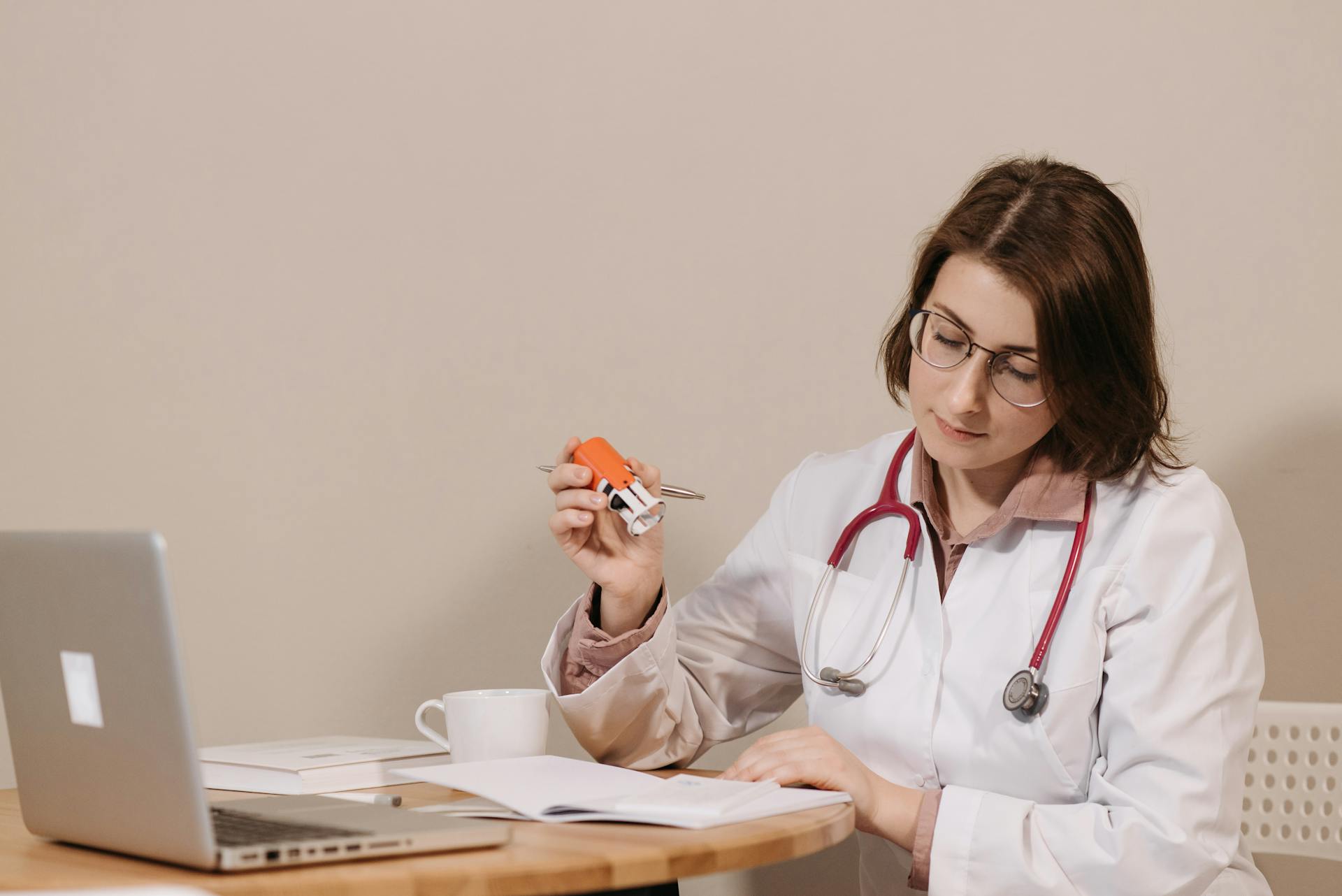 A focused female doctor reviews medical documents while sitting at her desk with a stethoscope.