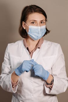 Female healthcare worker in white coat and face mask with gloves, focusing on protection and prevention.