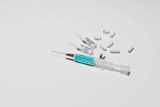 Close-up of a syringe, capsules, and ampoules on a white surface, representing medical treatment.