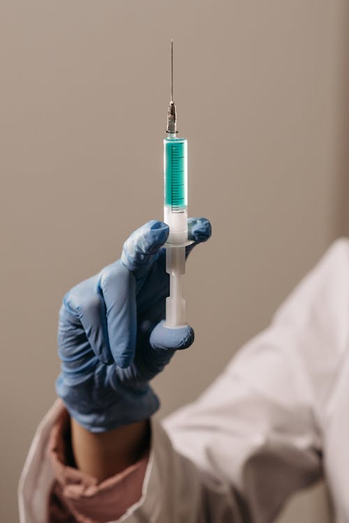 Person in White Scrub and Blue Latex Glove Holding Syringe