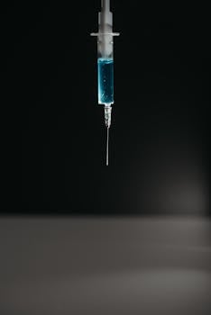 Close-up of syringe with blue liquid suspended on black backdrop.