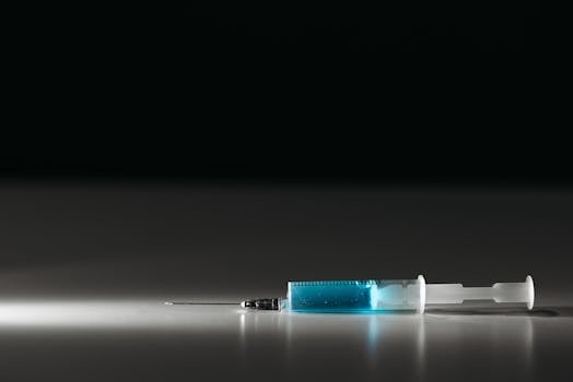 Detailed shot of a syringe with blue liquid on a reflective surface, captured in low light.