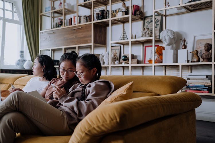 Girls Sitting On The Couch While Looking At The Phone