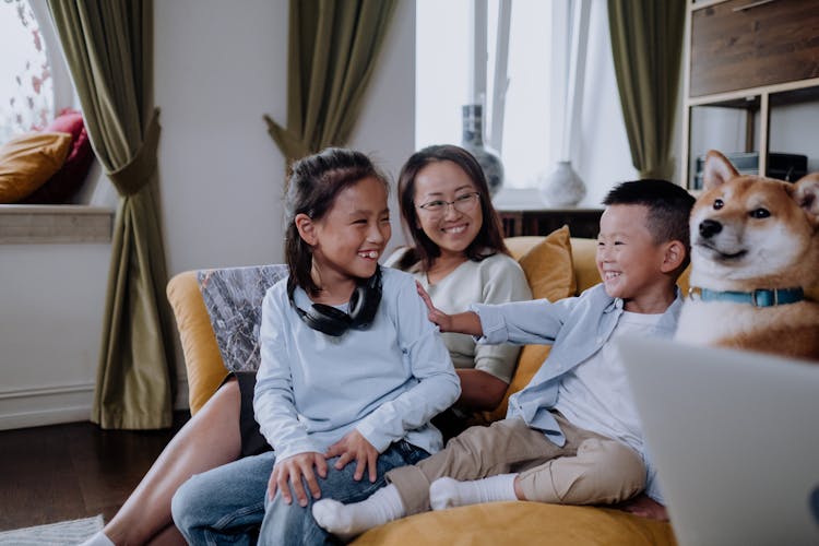 A Happy Family Sitting On The Couch While Playing With Their Dog