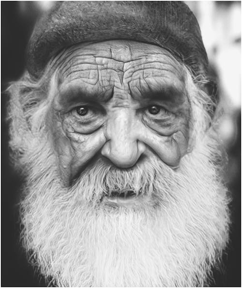 A Grayscale Photo of an Elderly Man with Full Beard on His Face
