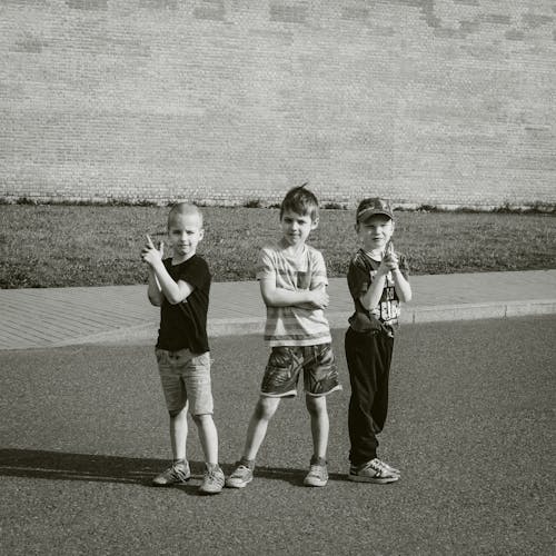A Grayscale Photo Kids Posing while Standing on the Street