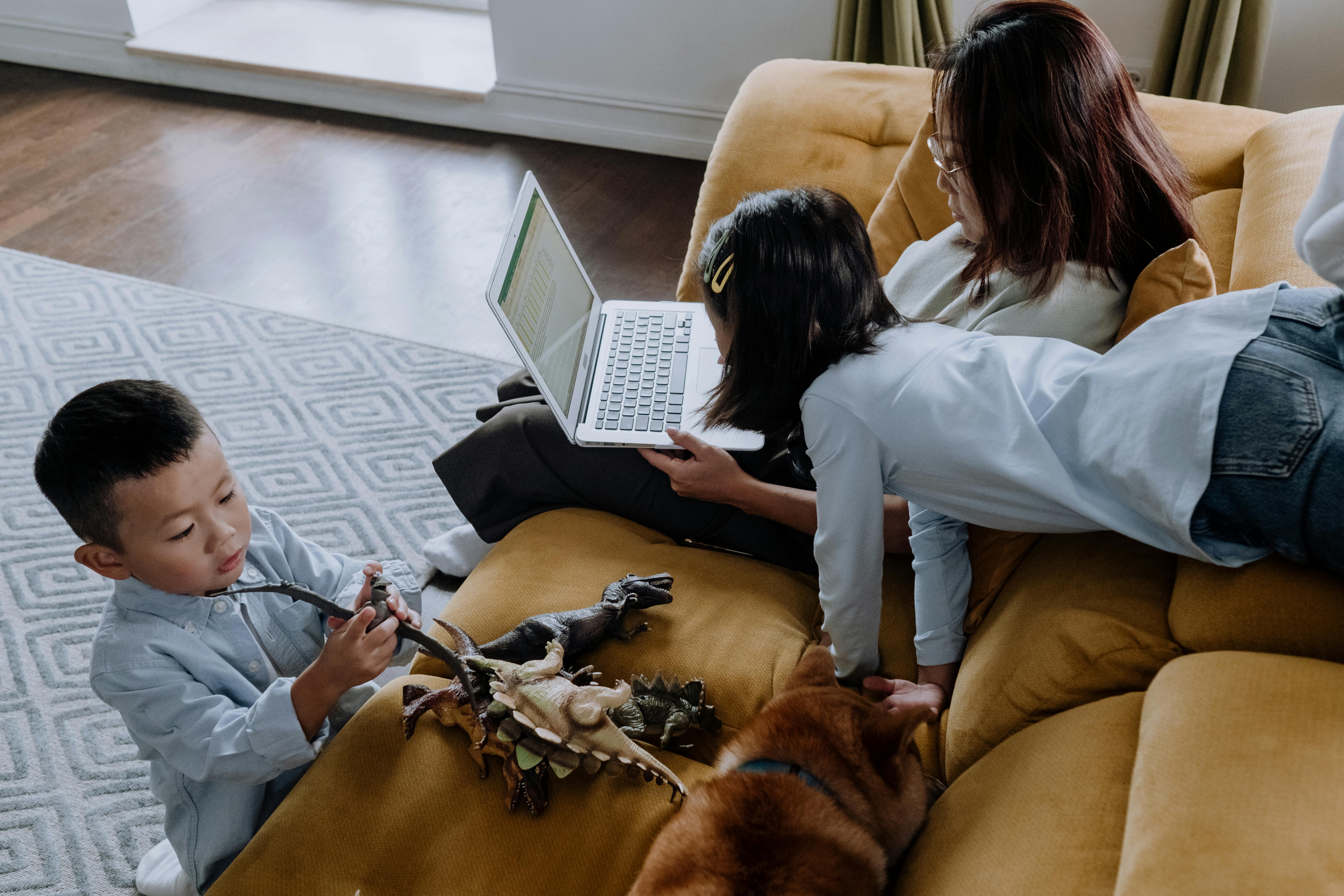 a woman using her laptop with her kids playing beside her