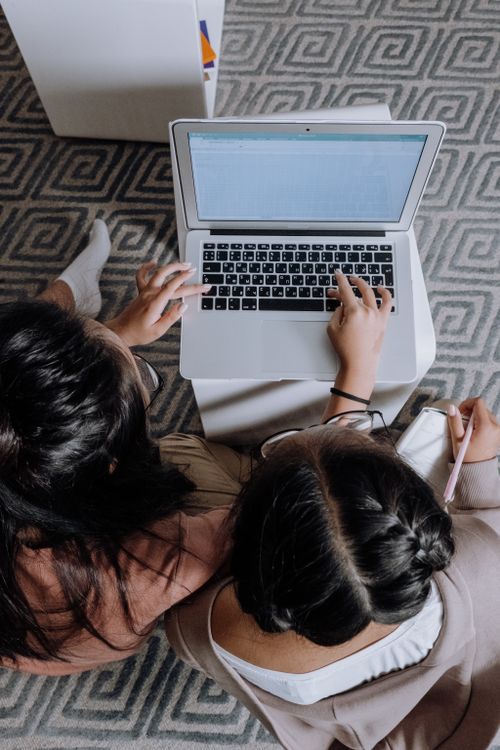 Free Two teenage girls sit together at home, focused on a laptop for study or homework. Stock Photo