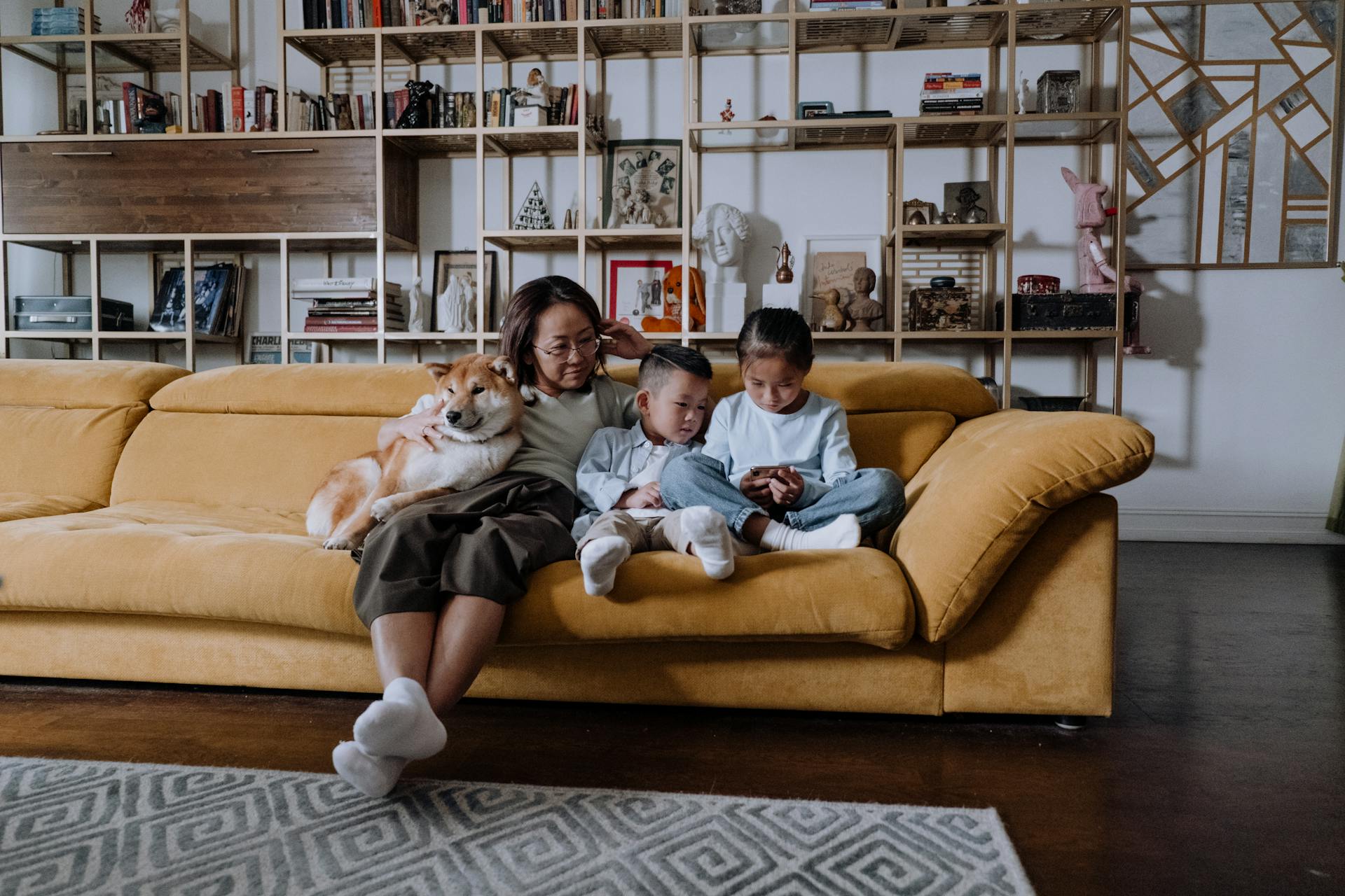 Mother and Two Children Sitting on Sofa with Shiba Inu Dog