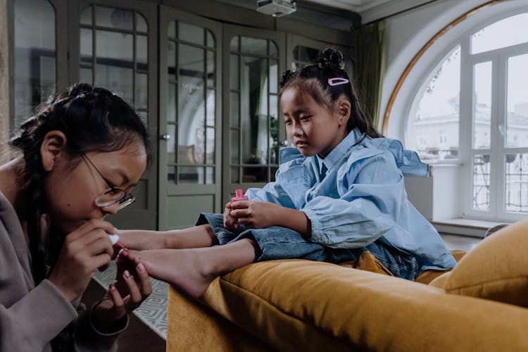 A Young Woman Applying A Nail Polish On Her Sister's Foot