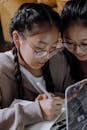 A Two Girls Wearing Eyeglasses While Writing