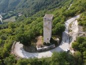 Drone view of ancient tall stone tower surrounded by rural road loop and located on verdant forested hill slope on sunny summer day