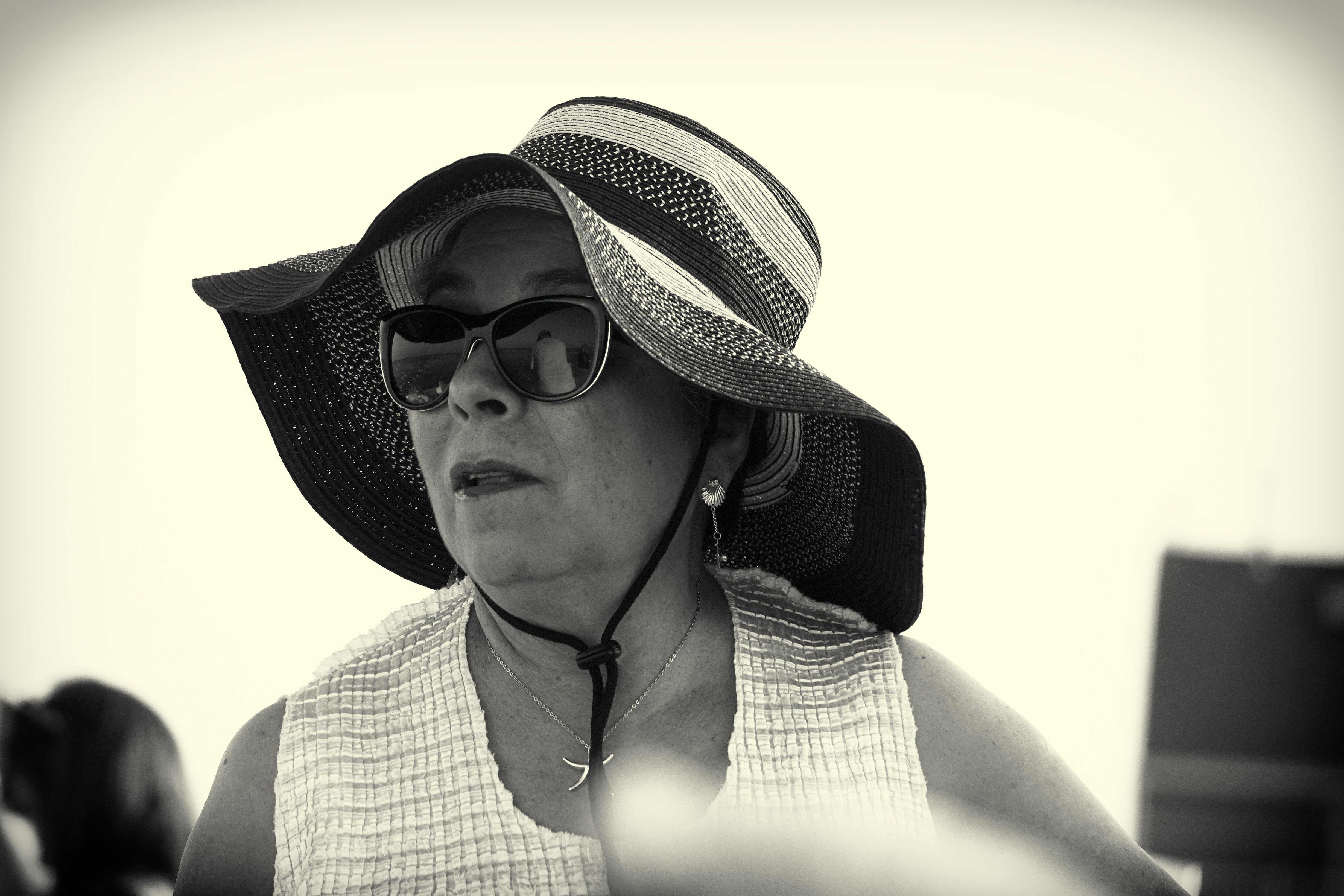 A fashionable woman wearing a large sun hat and sunglasses, captured in black and white.