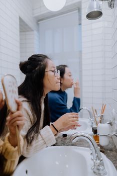 Teenage girl applying makeup in a stylish bathroom, looking in the mirror, showcasing daily beauty routine.