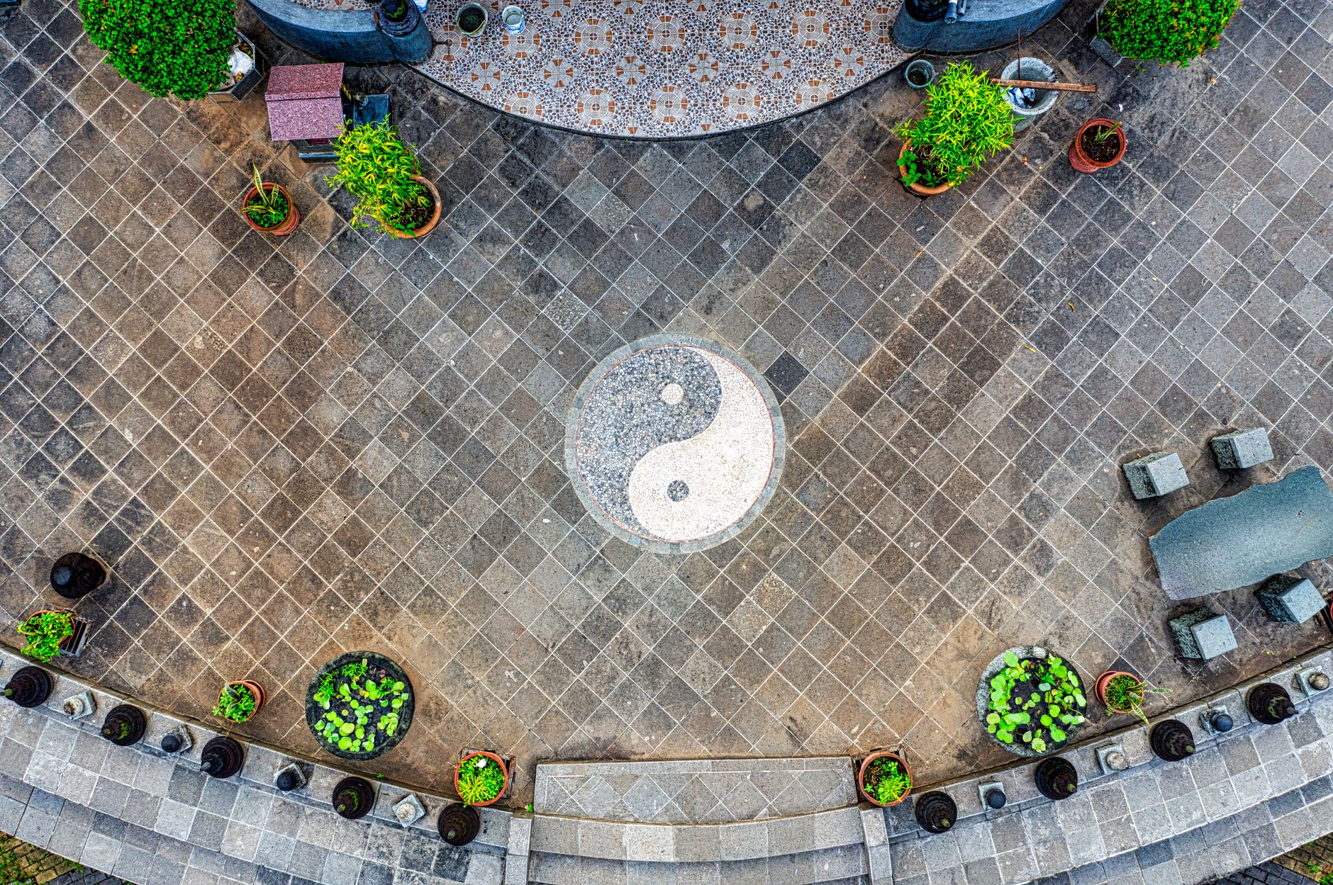 From above of inner yard with green potted plants and yin and yang symbol placed on paved walkway in daytime