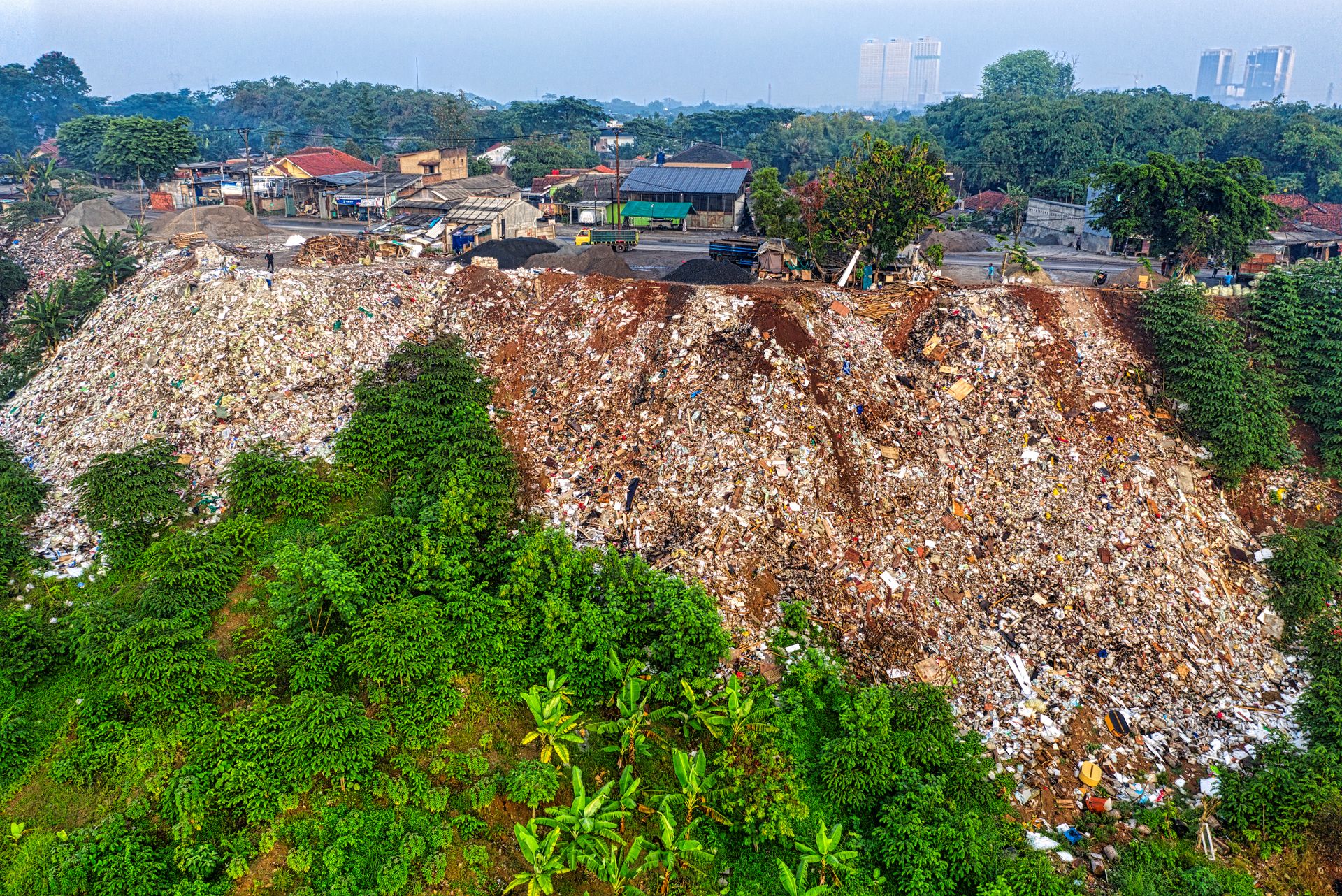 Slope of hill covered with garbage placed near town in daytime